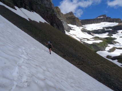 A hiker crosses a snowfield using trek poles